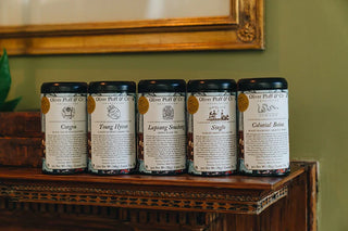 5 black tea tins with white label sitting on wooden shelf, green wall behind