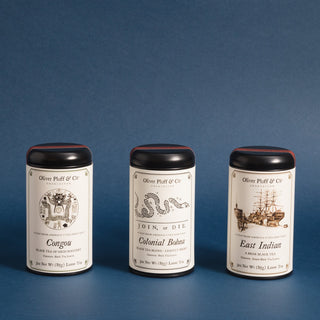 three black tea tins with black and white graphics of sailing ship, a snake and and flowery design against a blue background