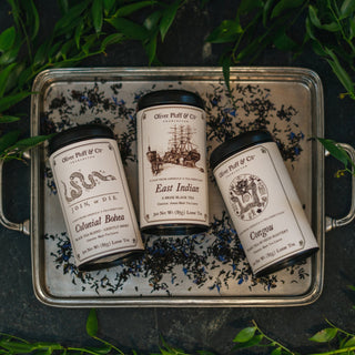 three tins of tea on silver tray surrounded by loose tea