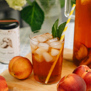 Glass of iced tea with peaches and a straw on a wooden board.