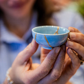 Person holding a small blue ceramic cup with gold accents
