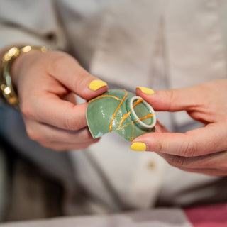 two hands repairing a broken bowl with using gold adhesive